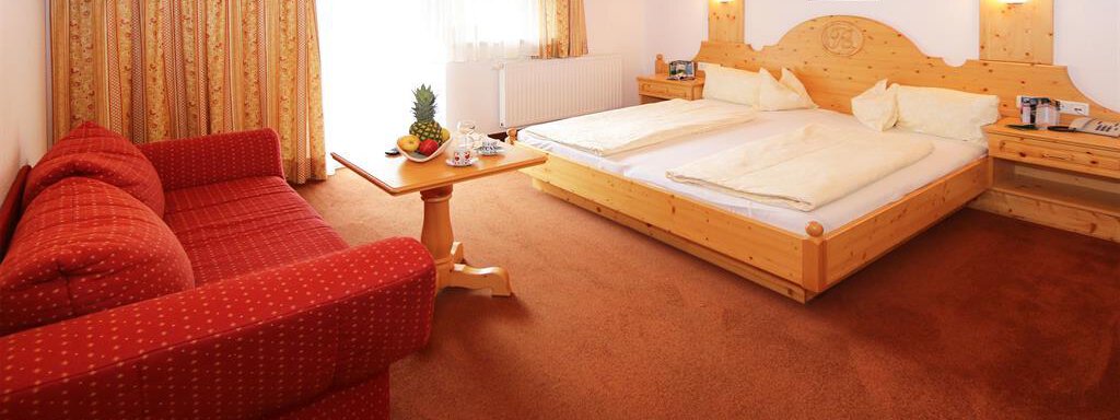 App1_Zimmer03 A cozy bedroom with two single beds and wooden details. A red couch and a small table with fruit complete the decor. - Ferienhaus Waldele - Sölden