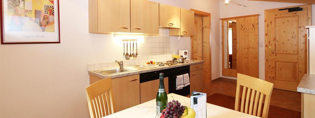 A bright kitchen with wooden shelves and modern equipment. Fresh fruit and a bottle of champagne are on the table. - Ferienhaus Waldele - Sölden