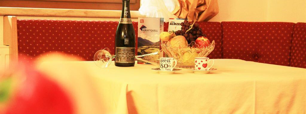 A beautifully set table with a bottle of sparkling wine and fresh fruit. The cozy atmosphere is accentuated by the red cushions and the daylight. - Ferienhaus Waldele - Sölden