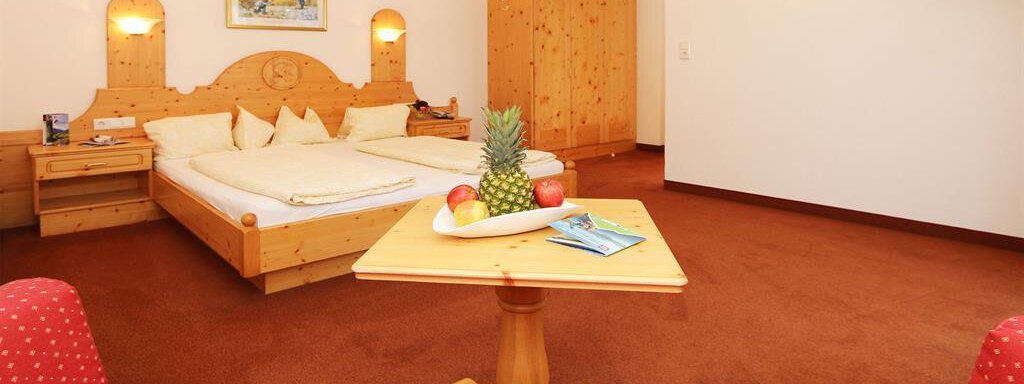 App2_Zimmer03 A cozy bedroom with a large bed and wooden furniture. There is a fruit bowl on the table, and a television is visible in the background. - Ferienhaus Waldele - Sölden