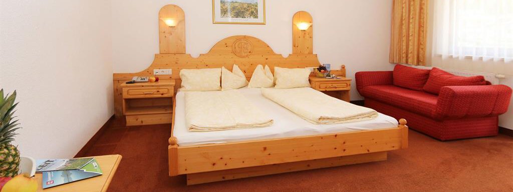 A cozy bedroom with a double bed and a red sofa. The room has wooden details and large windows that let in plenty of light. - Ferienhaus Waldele - Sölden