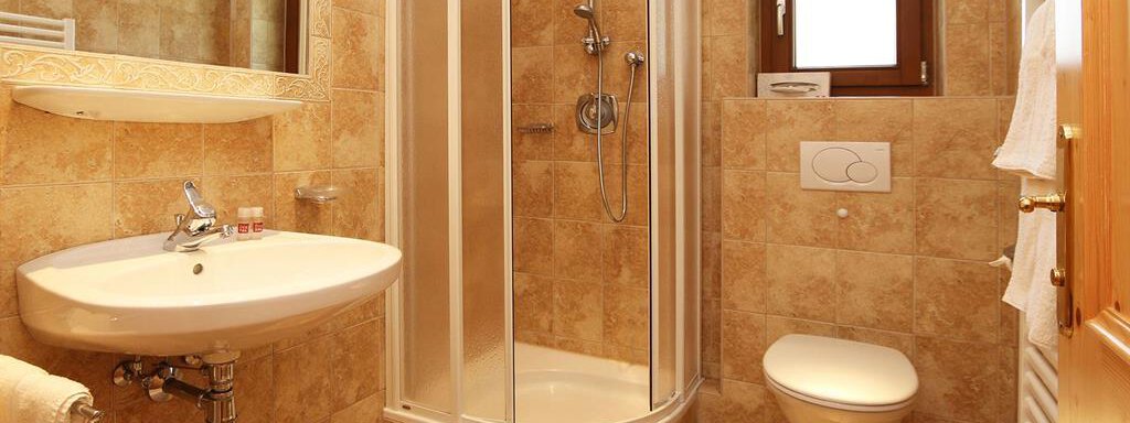 A modern bathroom with a shower, a sink, and a toilet. The walls are in warm shades and there are large mirrors. - Ferienhaus Waldele - Sölden