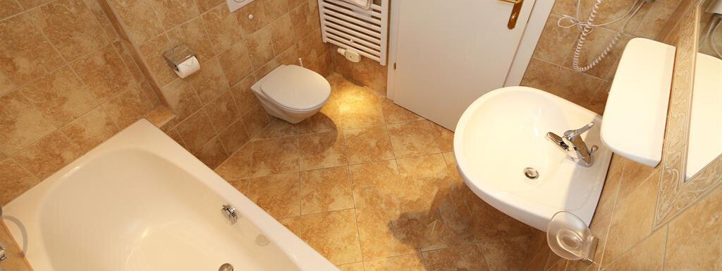 A modern bathroom with a bathtub, a sink, and a toilet. The walls are tiled in warm brown tones. - Ferienhaus Waldele - Sölden