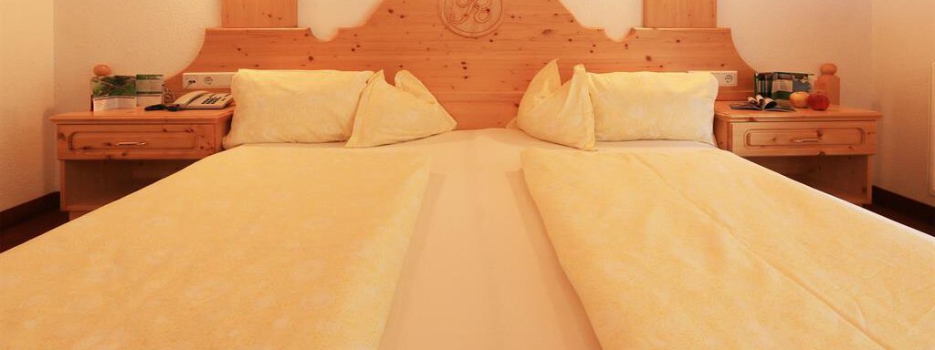 App1_Zimmer02 A cozy double room with two beds and light bedspreads. The walls are decorated with wooden paneling and soft lights. - Ferienhaus Waldele - Sölden
