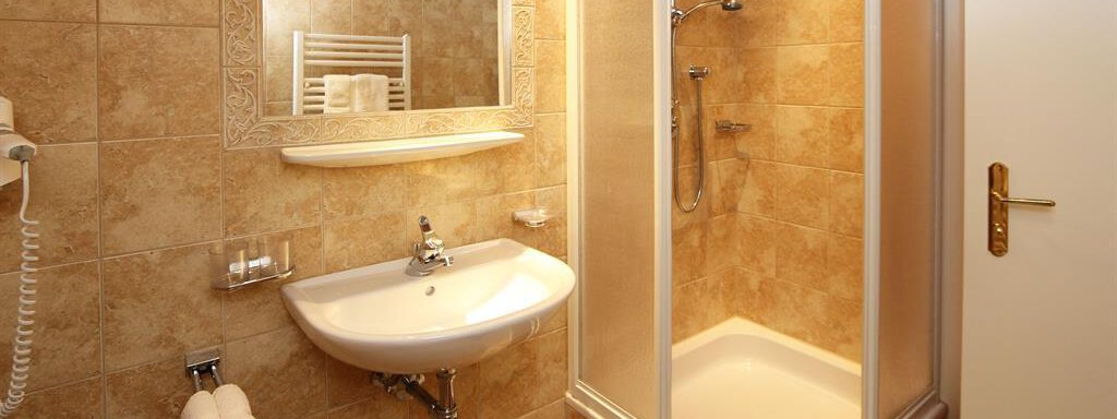 A modern bathroom with a shower, a sink, and a large mirror. The walls are decorated with light tiles in neutral tones. - Ferienhaus Waldele - Sölden