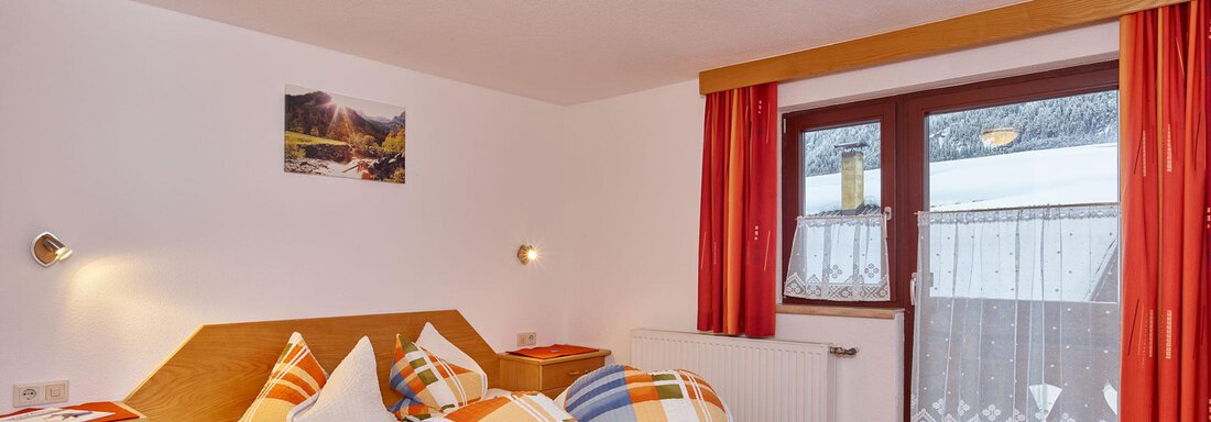 A cozy bedroom with a double bed and colorful cushions. There is a balcony with a view of the surroundings. - Ferienhof Paulelas - Sölden