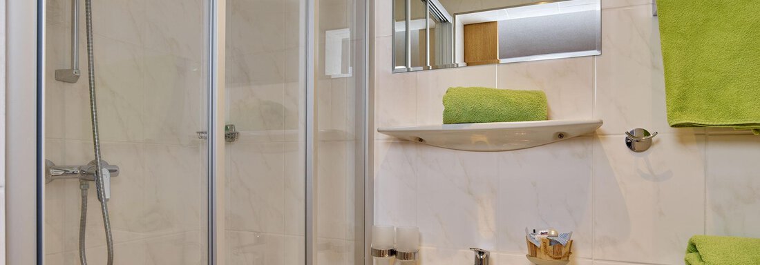 A modern bathroom with a shower cubicle and a sink. Green towels provide a fresh splash of color. - Ferienhof Paulelas - Sölden