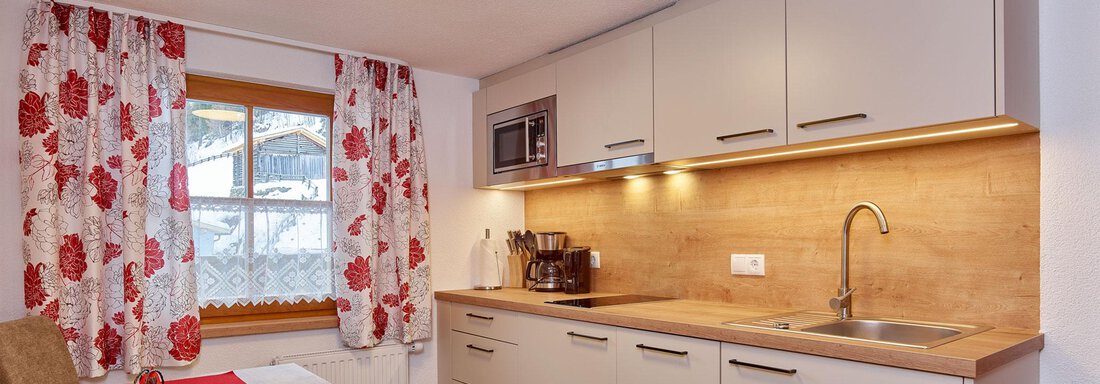 Appartement II | © Klocker Rebecca, Ferienhof Paulelas (CC C) A modern kitchen with bright wooden countertops and white furniture. The room is cheerful with red curtains and natural light. - Ferienhof Paulelas - Sölden