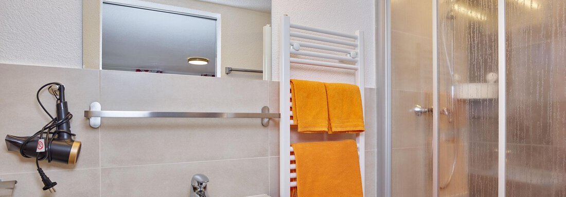 A modern bathroom with a shower and a sink. Orange towels hang on a towel rack. - Ferienhof Paulelas - Sölden