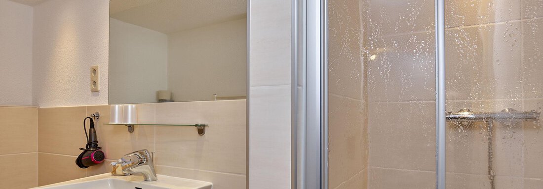 A modern bathroom with bright tiled flooring and a shower. There is a sink and a mirror on the wall. - Ferienhof Paulelas - Sölden