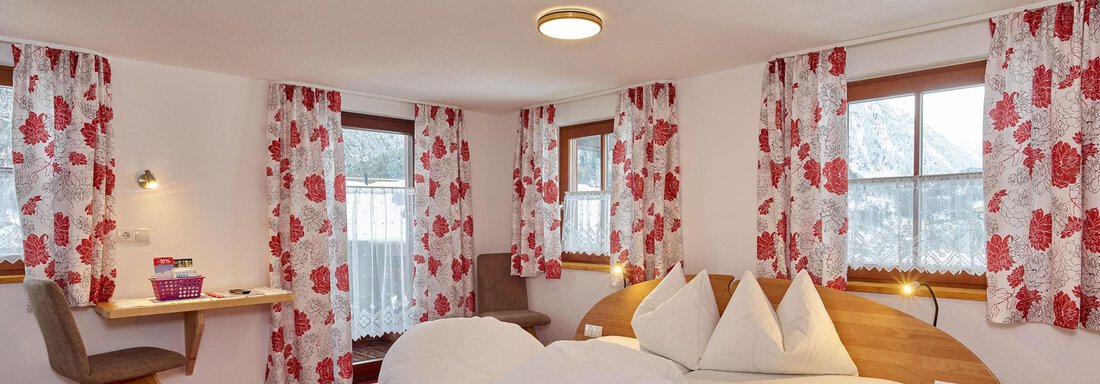 A cozy bedroom with a large bed and red carpet. The walls are decorated with white curtains that are patterned in red. - Ferienhof Paulelas - Sölden