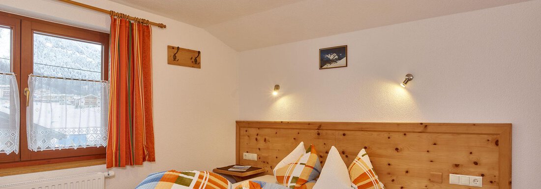 Appartement III | © Klocker Rebecca, Ferienhof Paulelas (CC C) A cozy bedroom with a large bed and colorful cushions. The warm colors and wooden furniture create an inviting atmosphere. - Ferienhof Paulelas - Sölden