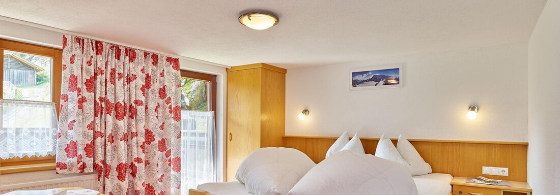 A cozy bedroom with a double bed and a table. The walls are bright and the windows let in plenty of light. - Ferienhof Paulelas - Sölden