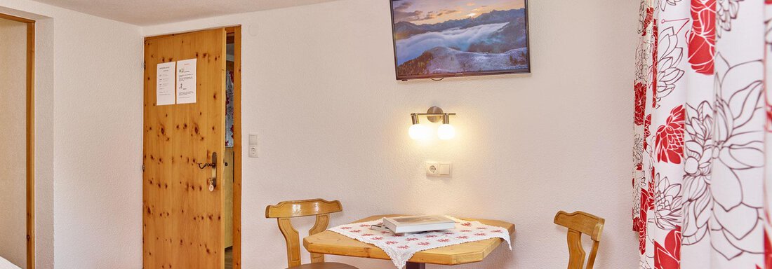 A cozy room with a small table and two chairs. The walls are decorated in light colors, and a picture hangs above the table. - Ferienhof Paulelas - Sölden