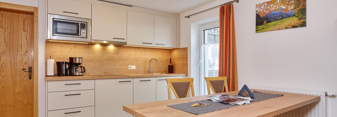 A modern kitchen corner with a dining table and two chairs. The furnishings include a microwave and a coffee machine in bright colors. - Ferienhof Paulelas - Sölden
