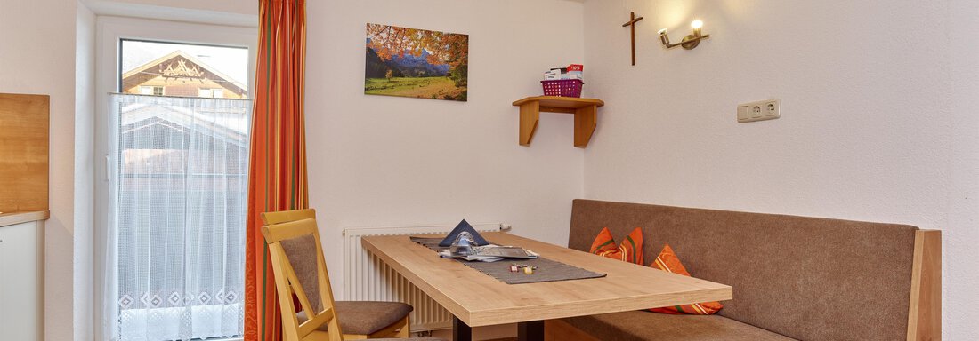 A cozy dining area with a rectangular table and beige armchairs. In the background, there are orange curtains and a wall decoration. - Ferienhof Paulelas - Sölden