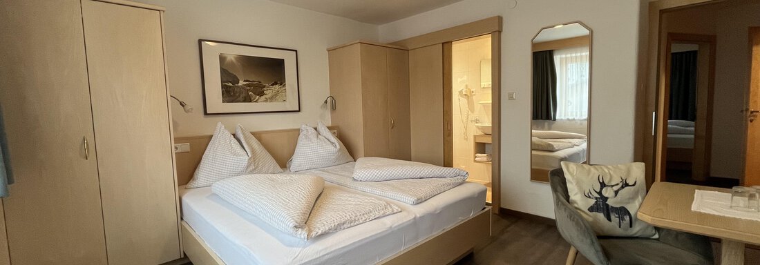 A cozy bedroom with a double bed and wooden cabinets. There is a table and chairs, as well as natural lighting from a window. - Franzele Appartements & Zimmer - Sölden