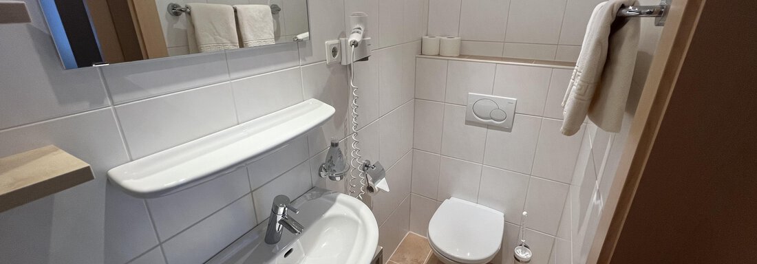 A modern bathroom with white tiles and a beautiful, bright decor. It features a sink, a toilet, and towels. - Franzele Appartements & Zimmer - Sölden