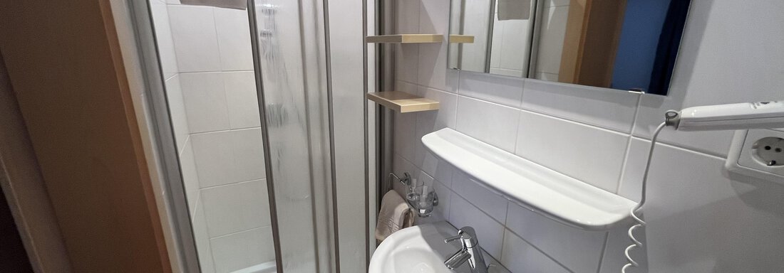 A modern bathroom with a shower cubicle and a vanity. The walls are brightly tiled and the fixtures are functional. - Franzele Appartements & Zimmer - Sölden