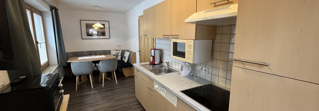 Modern kitchen with wooden cabinets and a cooking area. A dining area with chairs is visible in the background. - Franzele Appartements & Zimmer - Sölden