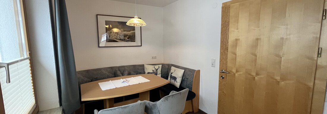 A bright dining area with a wooden table and cozy chairs. The large windows provide plenty of daylight. - Franzele Appartements & Zimmer - Sölden