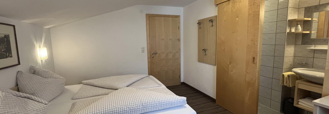 A cozy bedroom with a double bed and wood paneling. On the right is a modern bathroom with a shower and sink. - Franzele Appartements & Zimmer - Sölden