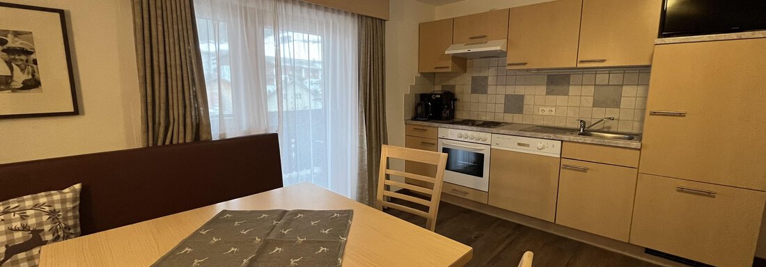 A modern kitchen with a dining area. The image shows a bright room with hardwood flooring and large windows. - Franzele Appartements & Zimmer - Sölden