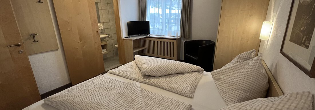 A cozy hotel room with two single beds and modern wooden furniture. There is a window with a view and a television in the room. - Franzele Appartements & Zimmer - Sölden