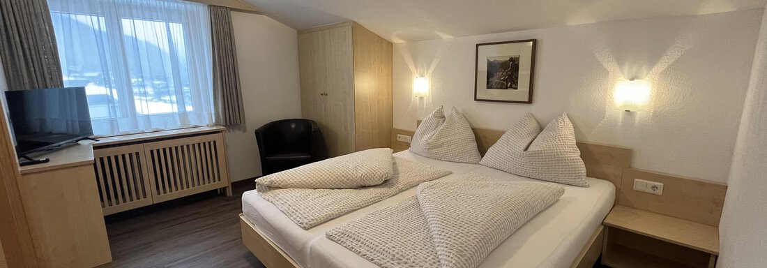 A cozy hotel room with a double bed and two pillows. There is a window with curtains and a television in the room. - Franzele Appartements & Zimmer - Sölden