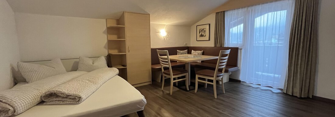 A cozy room with a single bed and a dining area. Large windows provide plenty of light. - Franzele Appartements & Zimmer - Sölden