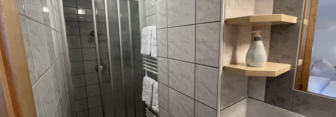 A modern bathroom with tiled walls and a shower. Towels and hygiene products are neatly arranged. - Franzele Appartements & Zimmer - Sölden