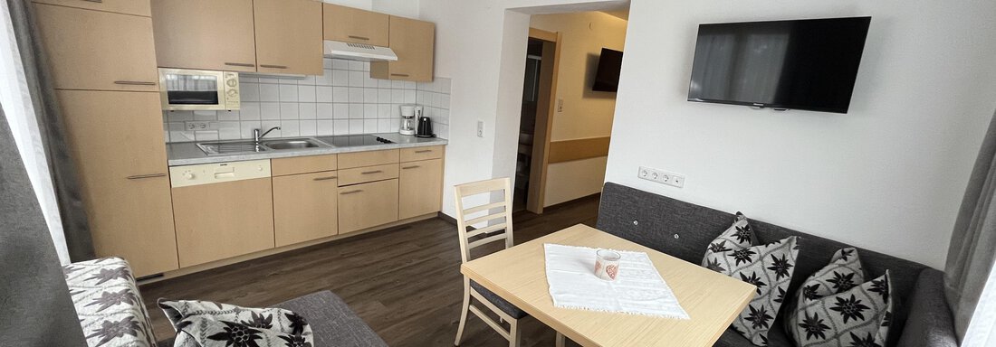 A modern apartment with a kitchenette and a cozy seating area. The table is placed in the center and a TV is mounted on the wall. - Franzele Appartements & Zimmer - Sölden