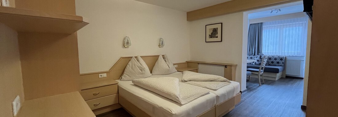 A simple room with two beds and modern furniture. There is a desk and a television, as well as large windows that let in natural light. - Franzele Appartements & Zimmer - Sölden