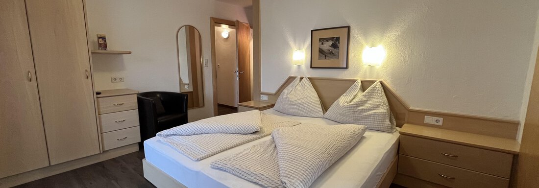 A cozy bedroom with a double bed and wooden cabinets. The walls are light, and the room feels inviting and tidy. - Franzele Appartements & Zimmer - Sölden
