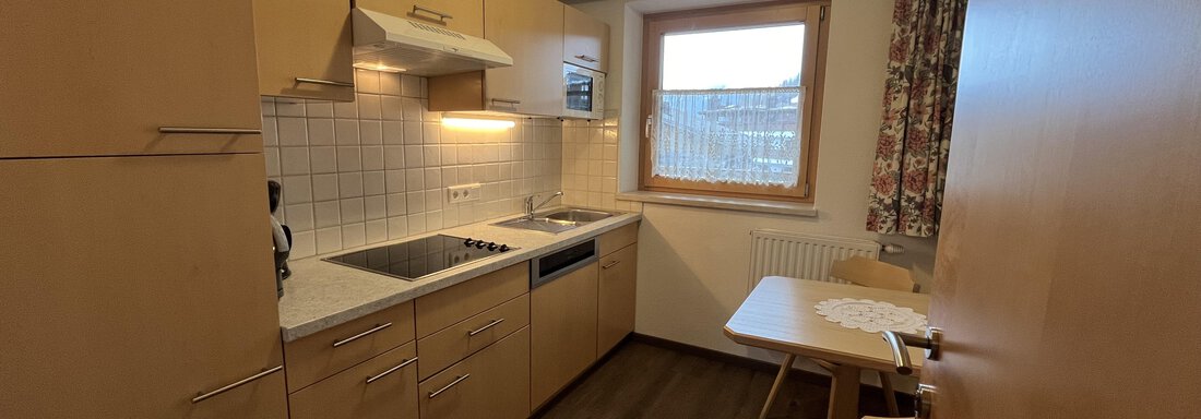 A modern kitchen with wooden cabinets and a small table. The window lets in a lot of daylight. - Franzele Appartements & Zimmer - Sölden