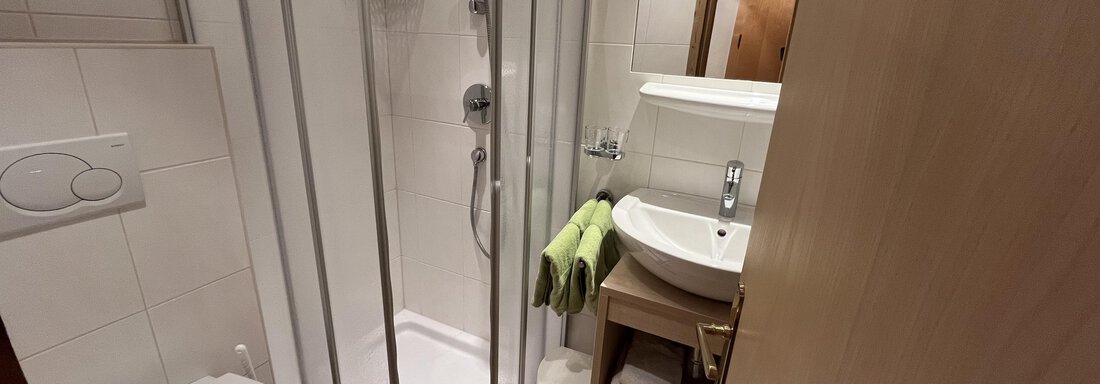 A modern bathroom with a shower, sink, and a toilet. Towels in fresh colors are placed on a shelf. - Franzele Appartements & Zimmer - Sölden