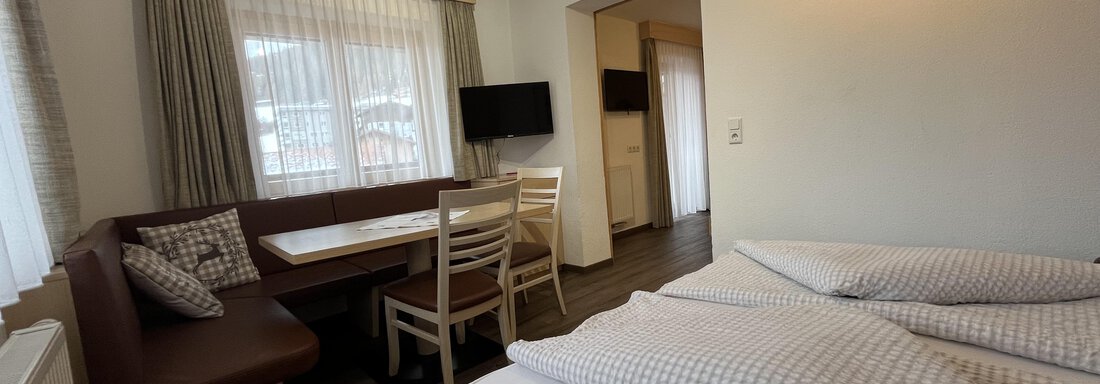 A cozy room with a double bed and a dining area. Large windows provide plenty of daylight. - Franzele Appartements & Zimmer - Sölden
