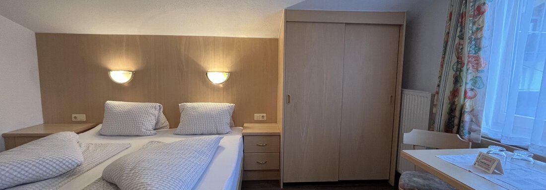 A cozy bedroom with two single beds and warm light. The room is simply and modernly furnished, with a small table and chair. - Franzele Appartements & Zimmer - Sölden