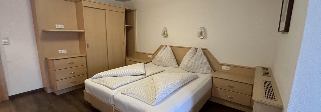 A simple hotel room with two single beds and wooden furniture. The walls are light, and there is a wardrobe as well as bedside tables. - Franzele Appartements & Zimmer - Sölden