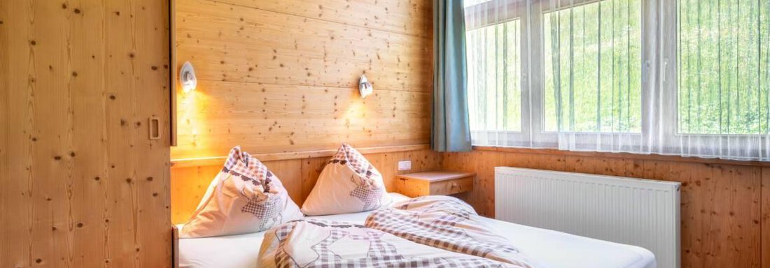408.3 A cozy bedroom with wooden paneling and a large bed. Large windows provide plenty of daylight and a view of the green landscape. - Garni Nadine - Sölden
