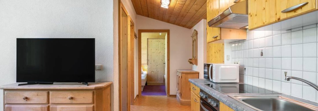 A modern kitchen with wooden cabinets and a television. The room has a bright, inviting look. - Garni Nadine - Sölden