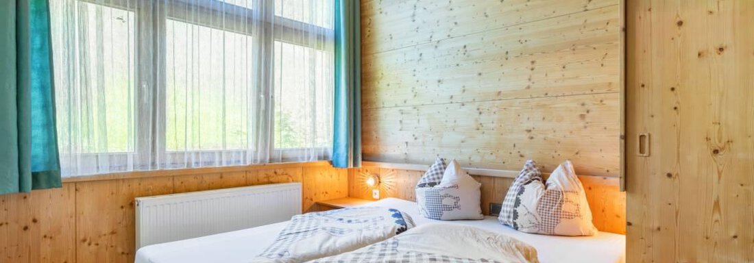 A cozy bedroom with wooden walls and large windows. The bed is inviting and decorated with pillows. - Garni Nadine - Sölden