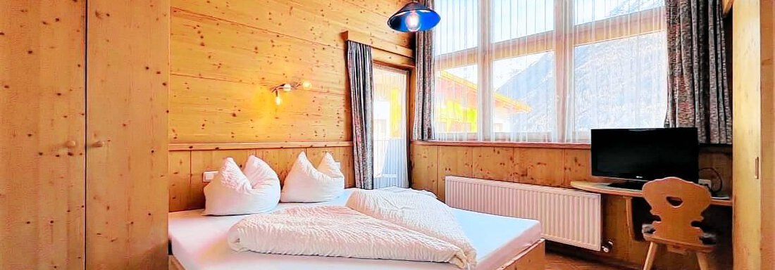 406 A cozy wooden bedroom with a large window and natural light. There is a double bed and a desk with a chair. - Garni Nadine - Sölden