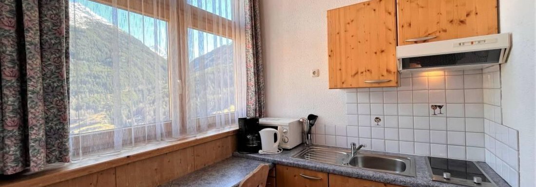 A bright kitchen with wooden cabinets and modern appliances. Large windows provide a view of the mountains. - Garni Nadine - Sölden