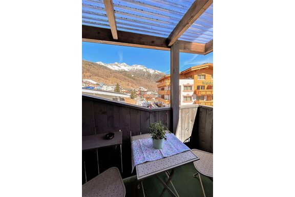 A cozy balcony with a table and two chairs. In the background, the snow-covered mountains and a beautiful view of the city can be seen. - Garni Nadine - Sölden