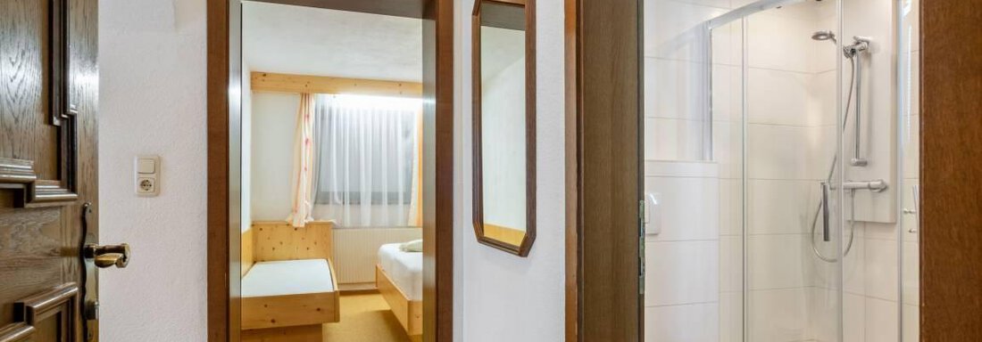 A bright hallway with wooden flooring and doors leading to a bedroom and a bathroom. The bathroom is modernly designed with a shower and a bright, friendly atmosphere. - Garni Nadine - Sölden