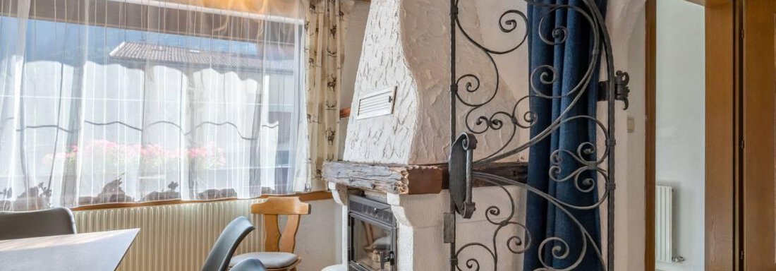 A cozy dining area with an open fireplace. The walls are light, and a dark curtain provides a nice contrast. - Garni Nadine - Sölden