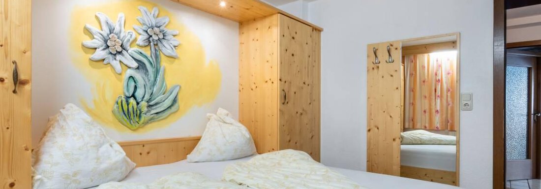 A cozy bedroom with a double bed and wooden shelves. A beautiful picture of flowers hangs on the wall. - Garni Nadine - Sölden