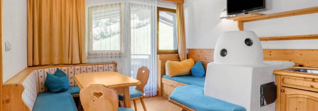 A cozy living area with wooden paneling and blue seating. A table is centrally located in the room, and large windows provide daylight. - Garni Nadine - Sölden