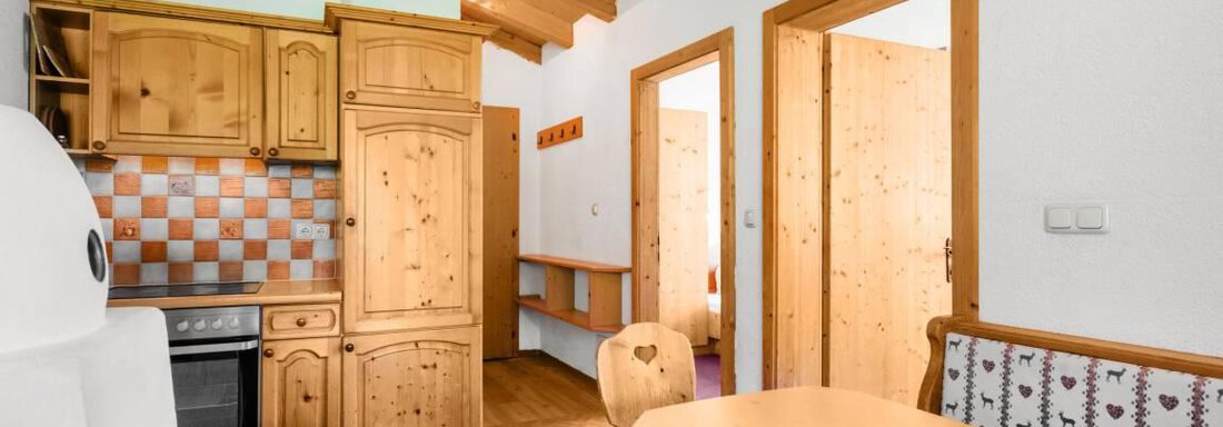 A cozy kitchen with wooden furniture and a dining table. The walls are light, and there are doors to other rooms. - Garni Nadine - Sölden
